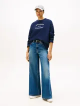 Buzo de felpa azul marino con cuello redondo, mangas largas y puños acanalados. Presenta un estampado frontal con el logo y letras de la marca Tommy Hilfiger en color blanco.