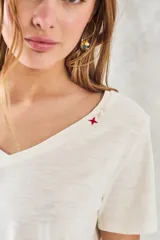Remera básica de algodón peinado color marfil, de manga corta y cuello en V, con detalle de pequeño bordado rojo en el escote.