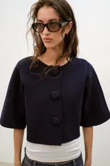 Chaqueta corta de punto color azul marino, de cuello redondo, manga por debajo del codo y cierre frontal con botones forrados al tono.