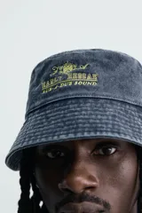 Sombrero tipo bucket de algodón con efecto lavado, color azul oscuro, con bordado frontal en tono amarillo que incluye la inscripción "Early Reggae Rub-A-Dub Sound". Cuenta con ala ancha con pespuntes decorativos.