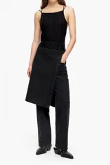 Conjunto de denim negro compuesto por un pantalón de corte recto y una falda tipo pareo sobrepuesta de largo midi. El diseño presenta un acabado lavado y cierre frontal.