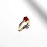 Anillo dorado con dije de cristal lágrima roja, con engarce de mesa y cristales claros alrededor.