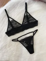 Conjunto de lencería compuesto por un bralette de encaje negro con diseño de tiras decorativas y una tanga colaless a juego con detalles de encaje y tiras ajustables.