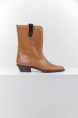 Bota de cuero color marrón con puntera fina y taco bajo. Presenta correas de cuero negro con apliques metálicos plateados.