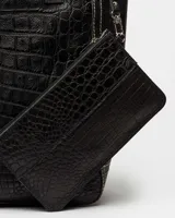 Bolso shopper negro de cuero con textura de cocodrilo, doble asa de hombro y dije colgante rectangular.