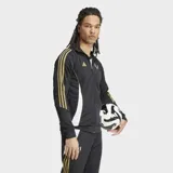 Campera deportiva de entrenamiento negra con cierre frontal y cuello alto. Presenta tres franjas doradas en las mangas y paneles laterales blancos. Lleva el logo de Adidas y el logo de Messi en dorado en el pecho.