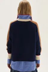 Sweater de tejido de punto azul marino con mangas raglan en color camel y puños con detalles en rojo y beige. Presenta un aplique bordado en el pecho con motivos de fantasía.