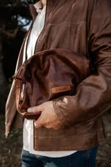 Necessaire de cuero natural marrón confeccionado artesanalmente, con diseño funcional y atemporal. Presenta laterales ajustables, cierre superior metálico y un parche frontal con el logo de la marca Soriame. Interior forrado y reforzado para mayor durabilidad.