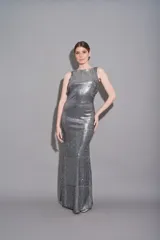 Vestido largo de fiesta plateado, bordado en lentejuelas, con espalda descubierta, sin mangas y escote redondo.