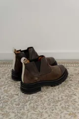 Bota tipo chelsea de punta redonda, confeccionada en una combinación de cuero texturizado y gamuza en tonos marrones. Presenta elásticos laterales negros y una suela track robusta de goma negra.
