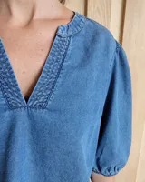 Blusa celeste de mangas 3/4 abullonadas, escote en V con detalle de bordado y lazo decorativo.