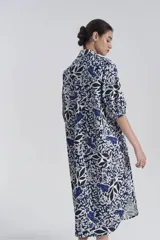 Vestido camisero midi con estampado floral en tonos azul, blanco y negro. Tiene cuello camisero, mangas 3/4 y abotonadura frontal parcial.