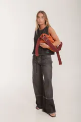 Bolso tipo hobo de gamuza color naranja quemado, con correa ancha de tela color bordó.