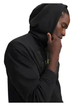 Hoodie Under Armour de color negro con capucha y cordones ajustables. Presenta un estampado gráfico frontal con el nombre de la marca en efecto camuflaje gris y el logo en color amarillo lima. Cuenta con un bolsillo tipo canguro y puños y bajo acanalados.