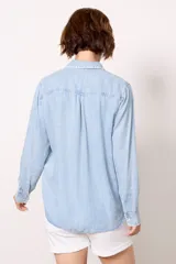 Camisa celeste de denim tencel, de corte holgado, con cuello clásico, cierre frontal con botones y bolsillo en el pecho con detalle bordado.