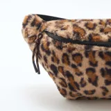 Riñonera de textura suave tipo peluche con estampado animal print de leopardo. Cuenta con cierre superior negro y correa ajustable.
