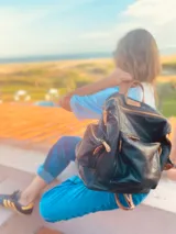 Mochila negra de cuero blando con herrajes dorados, correas marrones ajustables y cierre con cremallera.