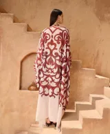 Kaftan largo de corte holgado con estampado abstracto en tonos bordó sobre fondo claro. Presenta escote en V profundo, mangas anchas tipo kimono y un cordón trenzado ajustable en la cintura con terminaciones de borlas.