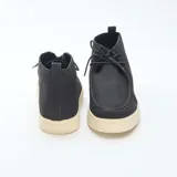 Zapatos tipo chukka de corte casual, con capellada en color negro y suela de goma en tono crema. Presentan cierre mediante cordones y una costura distintiva en la puntera.