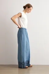 Pantalón de jean de corte holgado y pernera ancha, con cintura elástica y detalle de bordado oscuro con diseño floral y perforaciones en el bajo.