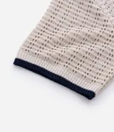 Camisa polo de manga corta, color beige claro, con textura de tejido abierto tipo ganchillo. Posee cuello y ribetes en las mangas en color azul marino.