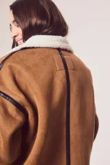 Campera marrón de gamuza sintética con cuello, puños y ruedo de piel sintética blanca. Presenta cierre frontal con cremallera, bolsillos laterales y detalles en cuero sintético negro.