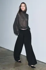 Blusa negra con estampado de lunares blancos, cuello redondo con lazadas y manga larga con puños ajustados. El bajo es ajustable con cordones.