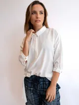 Blusa blanca de mangas 3/4 con cuello camisero, cierre frontal parcial con botones y detalle drapeado en el lateral.