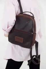 Mochila pequeña de cuero color marrón y beige, con bolsillo externo con cierre, manija superior, bolsillos laterales con broche imán y correas ajustables.