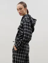 Camisa de manga larga con capucha, confeccionada en tejido liviano con estampado a cuadros. Presenta cierre frontal con botones y lazo regulable en la cintura.