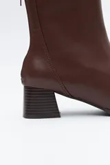 Bota corta de caña media color marrón oscuro, con puntera cuadrada y taco medio geométrico con textura acanalada. Presenta cierre de cremallera en la parte trasera y un ajuste tipo calcetín en la caña.