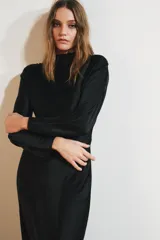 Vestido largo negro de tejido satinado, con cuello subido, manga larga y drapeado en los hombros. Presenta una abertura en la espalda con cierre de botones forrados a tono.