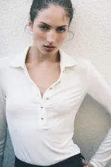 Remera polo de manga larga color blanco, confeccionada en tejido de punto acanalado. Presenta cuello clásico y tapeta frontal con botones dorados.