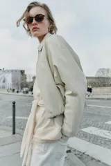 Chaqueta estilo bomber de cuero sintético en color beige, con cuello solapa, cierre frontal con cremallera, mangas largas y bajo elástico fruncido.