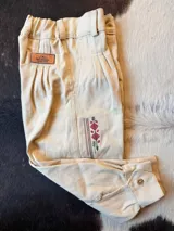 Bombacha de campo beige, con cintura elastizada y trabillas para cinturón. Presenta pinzas frontales, bolsillos laterales y un delicado bordado artesanal en la pierna. Los puños son ajustables con botón.