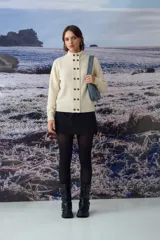 Cardigan de punto color crema con cuello alto y cierre frontal de botones oscuros. Presenta un diseño de textura acanalada en la franja central de los botones y mangas largas.