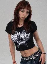 Remera tipo baby tee de corte ajustado, color negro, con estampado frontal en blanco de un corazón con alas y elementos urbanos.