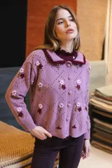 Saco de punto color rosa con bordados artesanales de flores. Presenta un cuello con detalle de volados en color bordó, cierre frontal con botones y diseño de calados en forma de rombos.