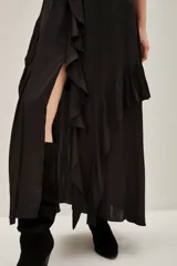 Vestido largo negro con escote en V y volados en el borde del escote y mangas. Presenta un corte peplum con elástico en la cintura y falda larga con abertura frontal y volados.