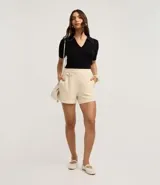 Blusa negra de punto con cuello polo, escote en V y mangas cortas. Detalle de mini perlas aplicadas en el cuello.