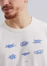 Remera de corte regular color beige con cuello redondo, mangas cortas y estampa frontal de pequeños nudos marineros en tono azul.