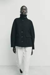 Abrigo corto de paño con mezcla de lana, color negro. Presenta cuello subido con cierre de botones, manga larga y dos bolsillos de plastrón con solapa en el frente. Cierre frontal con botones.