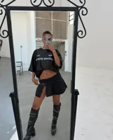 Minifalda de tiro bajo confeccionada en denim negro, con diseño plisado y detalle de hebilla frontal. Presenta un tajo lateral que aporta un estilo moderno y audaz.