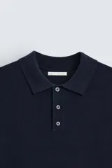 Polo de punto negro, manga corta, con cuello solapa y cierre frontal de tres botones. Presenta un calce regular y acabados en rib en mangas y ruedo.