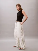 Pantalón parachute de nailon color crudo, de corte holgado, cintura elástica con cordón interior, puños con cordón y cremallera, cierre mediante botón y cremallera, diseño de bolsillo superpuesto y bordado de Calvin Klein en la cadera.