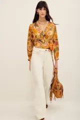 Camisa tipo cruzada (wrap) de manga larga con estampado floral multicolor en tonos mostaza y bordó. Cuenta con escote en V cruzado y detalle de lazo lateral con flor aplicada.