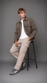Camisa tipo overshirt de manga larga con diseño de cuadros en tonos marrones y negros. Presenta cuello clásico, cierre frontal con botones y dos bolsillos frontales con solapa y botón en el pecho.