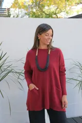 Sweater de punto color bordó, con cuello redondo, mangas largas y bolsillos frontales tipo parche. Presenta un corte holgado y diseño asimétrico con terminaciones en rib.