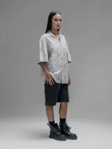 Camisa de manga corta color beige con cuello clásico y cierre de botones. Presenta un diseño de bordado calado con motivos florales y geométricos.