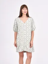 Vestido corto color verde claro con estampado de palmeras blancas en forma de abanico. Tiene escote en V con botones frontales y mangas cortas abullonadas.